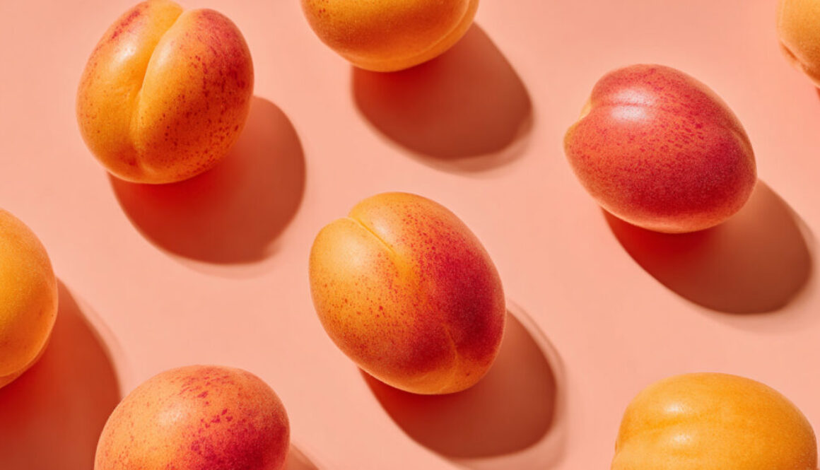 Free stock photo of fresh apricots casting soft shadows on a pastel salmon background, shot from top view