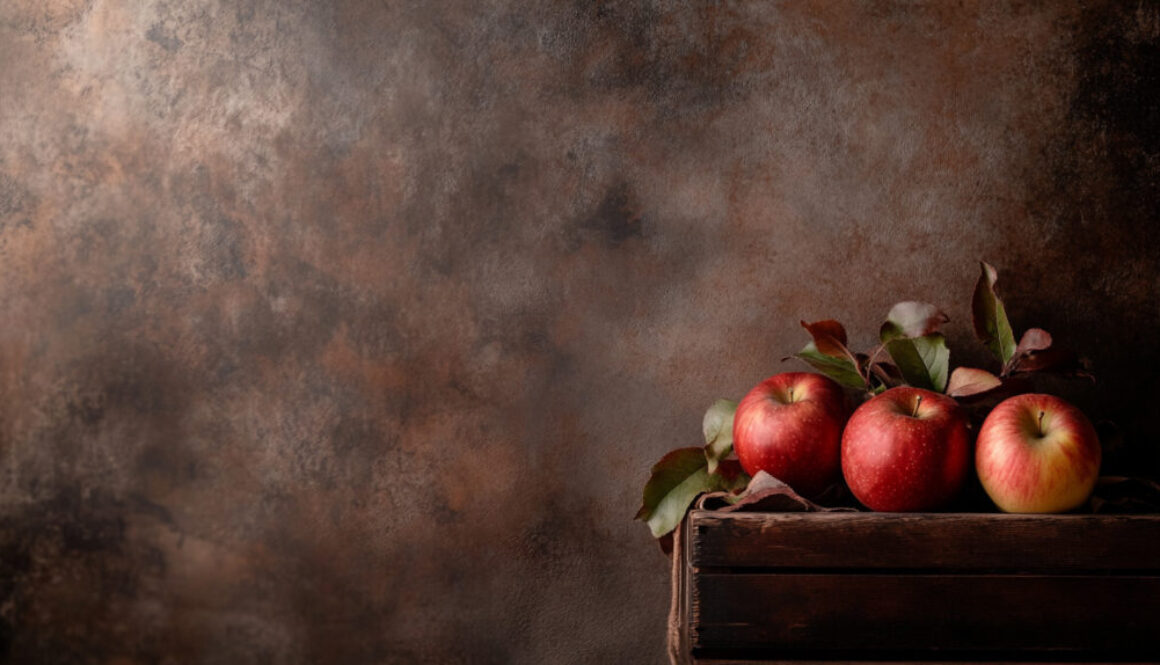 Three red apples in rustic wooden crate on warm brown background in 16:9 format
