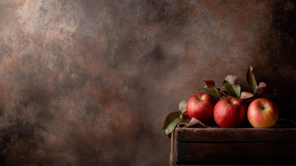 Three red apples in rustic wooden crate on warm brown background in 16:9 format