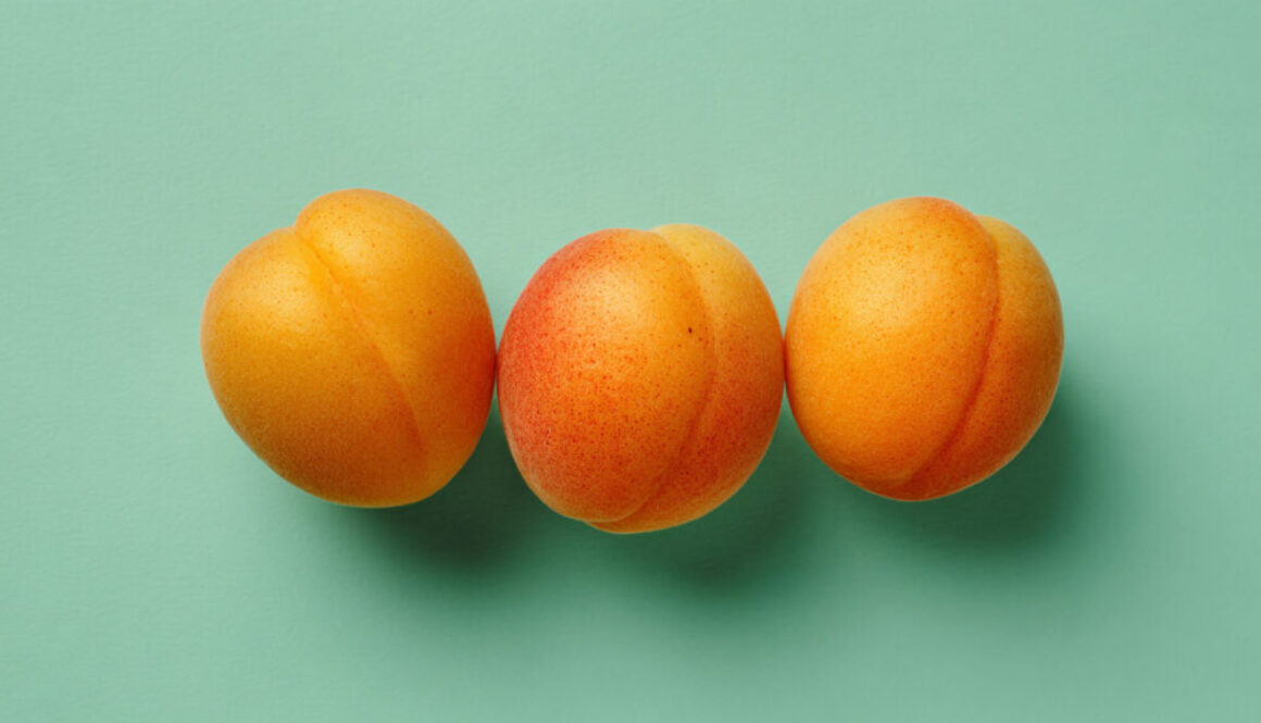 Three whole apricots aligned on mint green background, minimal fruit stock photo