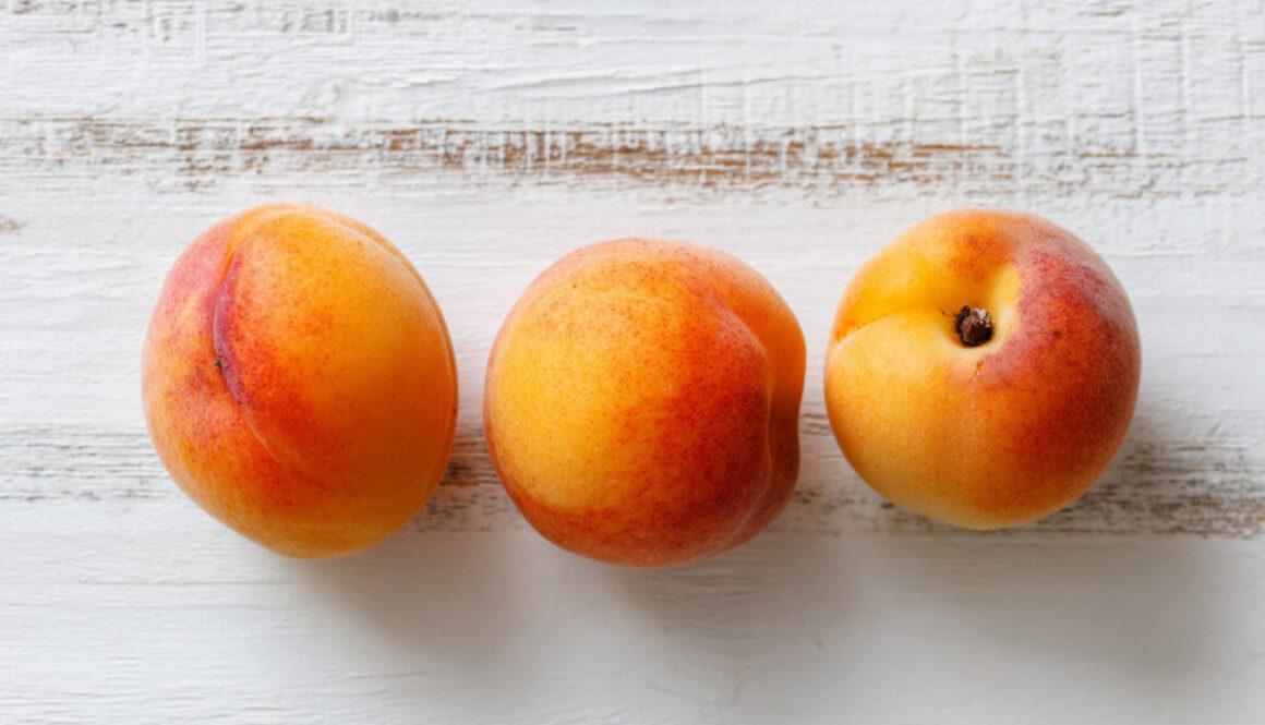 Three apricots on rustic white wood background, top view – free 16:9 image