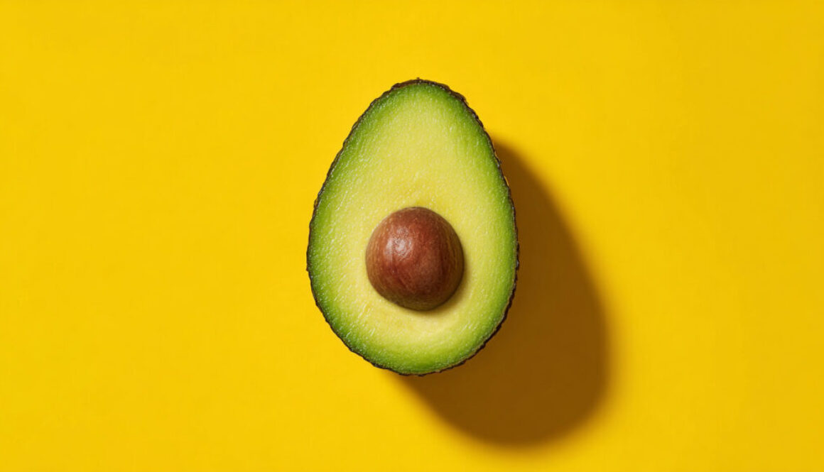 Half avocado with seed centered on yellow background, 16:9 image for commercial use