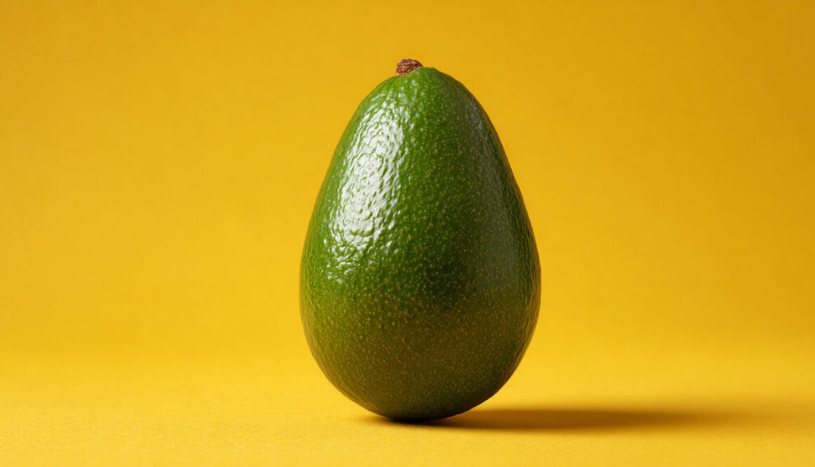 Whole green avocado centered on solid yellow background in 16:9 format