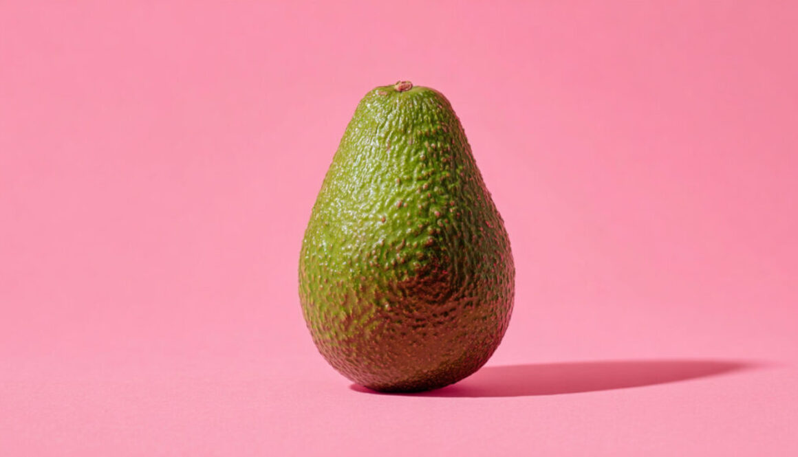 Front view of whole avocado standing upright on strawberry pink background in 16:9 format