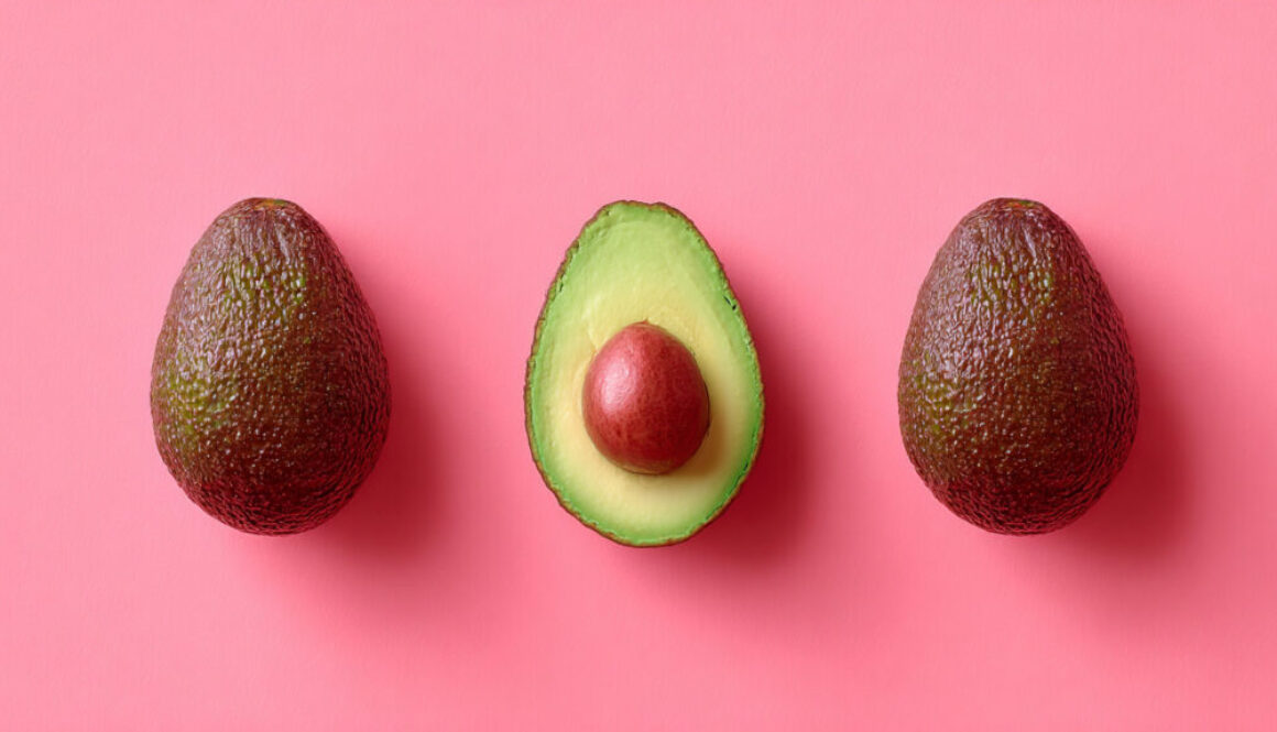 Top view of two whole avocados and one halved on strawberry pink background in 16:9 format