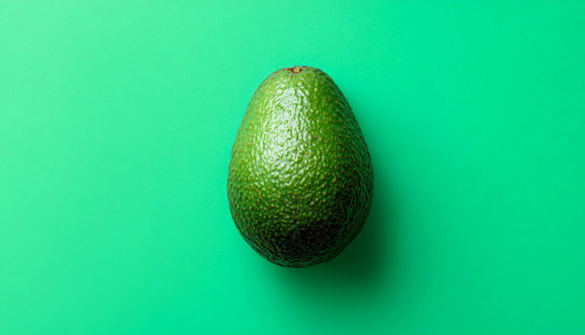Top view of whole avocado centered on turquoise background in 16:9 format
