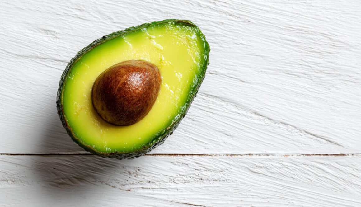 Top view of avocado half with seed on white wood background in 16:9 format