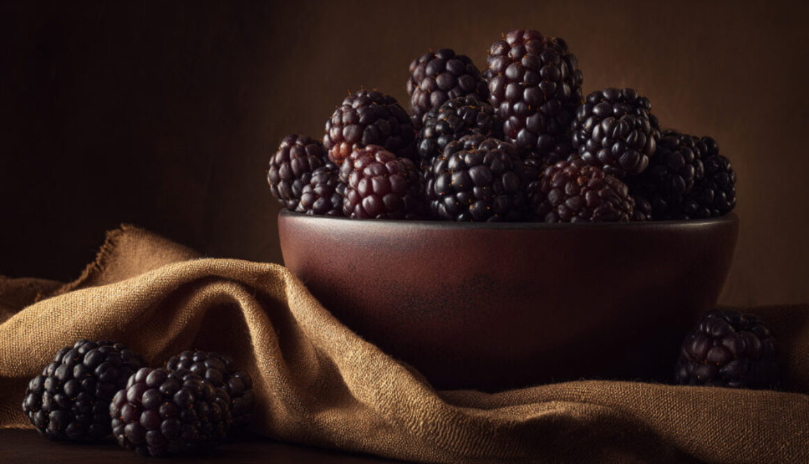 Rustic still life of fresh blackberries in a brown ceramic bowl on textured fabric, 16:9 format