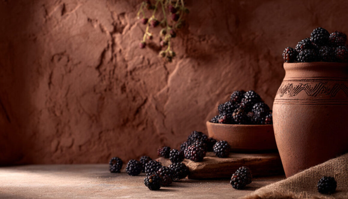 Rustic still life of blackberries in clay pots on terracotta background in 16:9 format