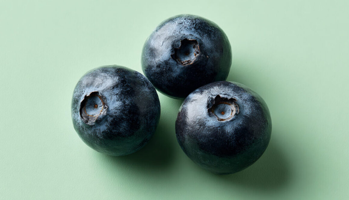 Three blueberries on pastel green background in minimal 16:9 format