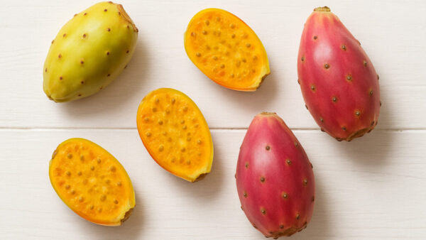 Top view of whole and halved cactus fruits on white wooden background in 16:9 format