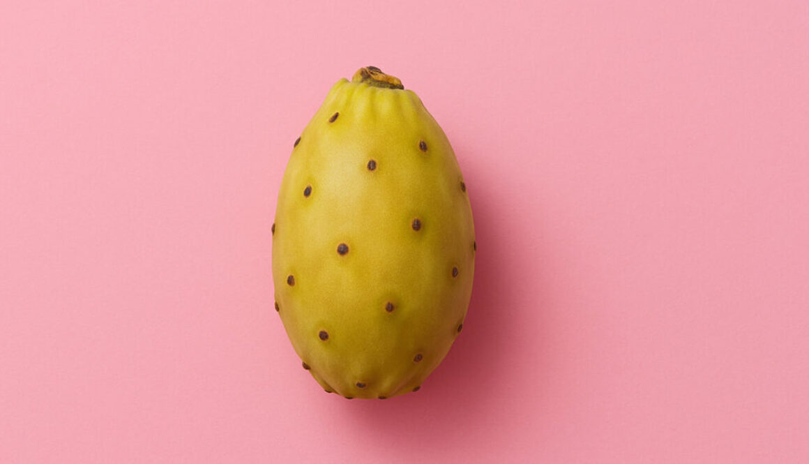 Single yellow cactus fruit centered on vibrant pink background in 16:9 format