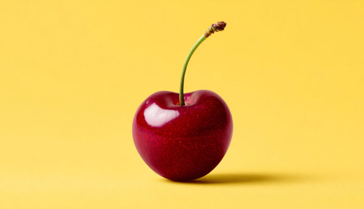 Single red cherry centered on yellow solid background in 16:9 format