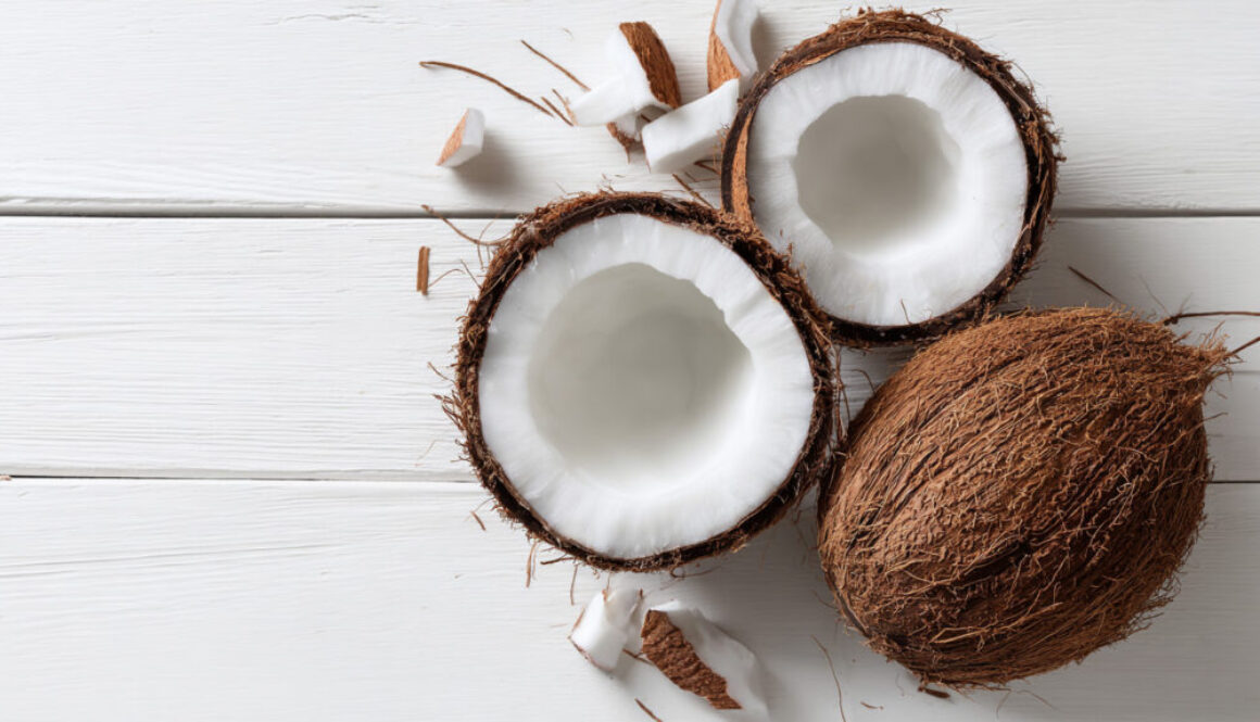 Flatlay of whole and halved coconuts with pieces on white wooden background in 16:9 format