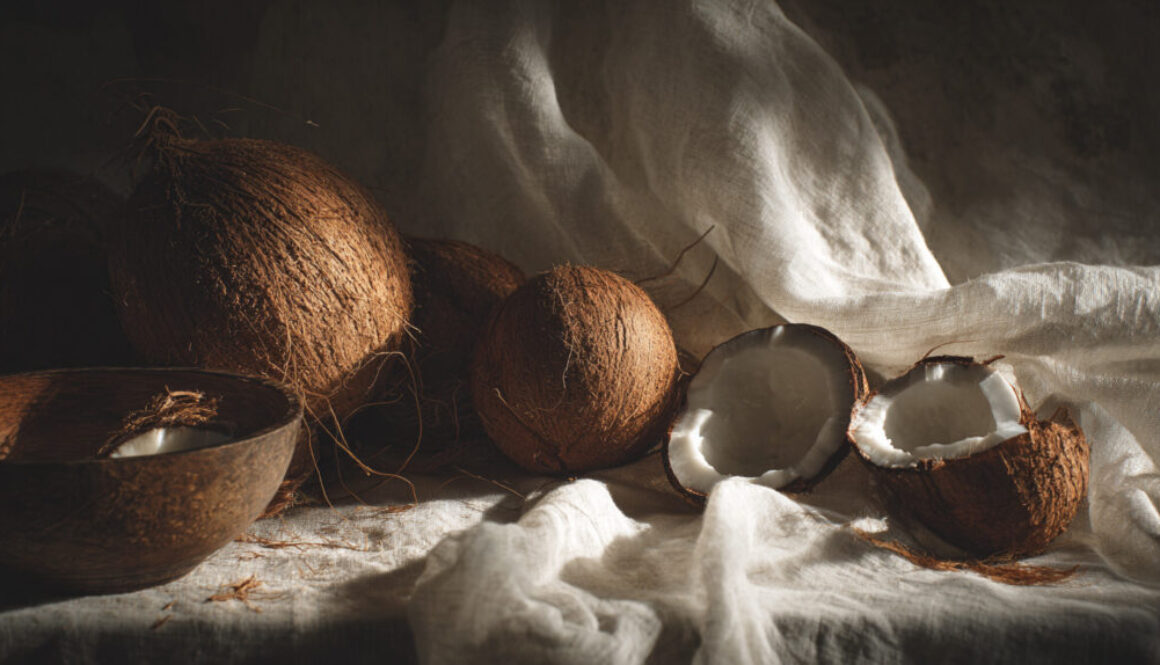 Still life with whole and halved coconuts placed on soft fabric with warm natural light
