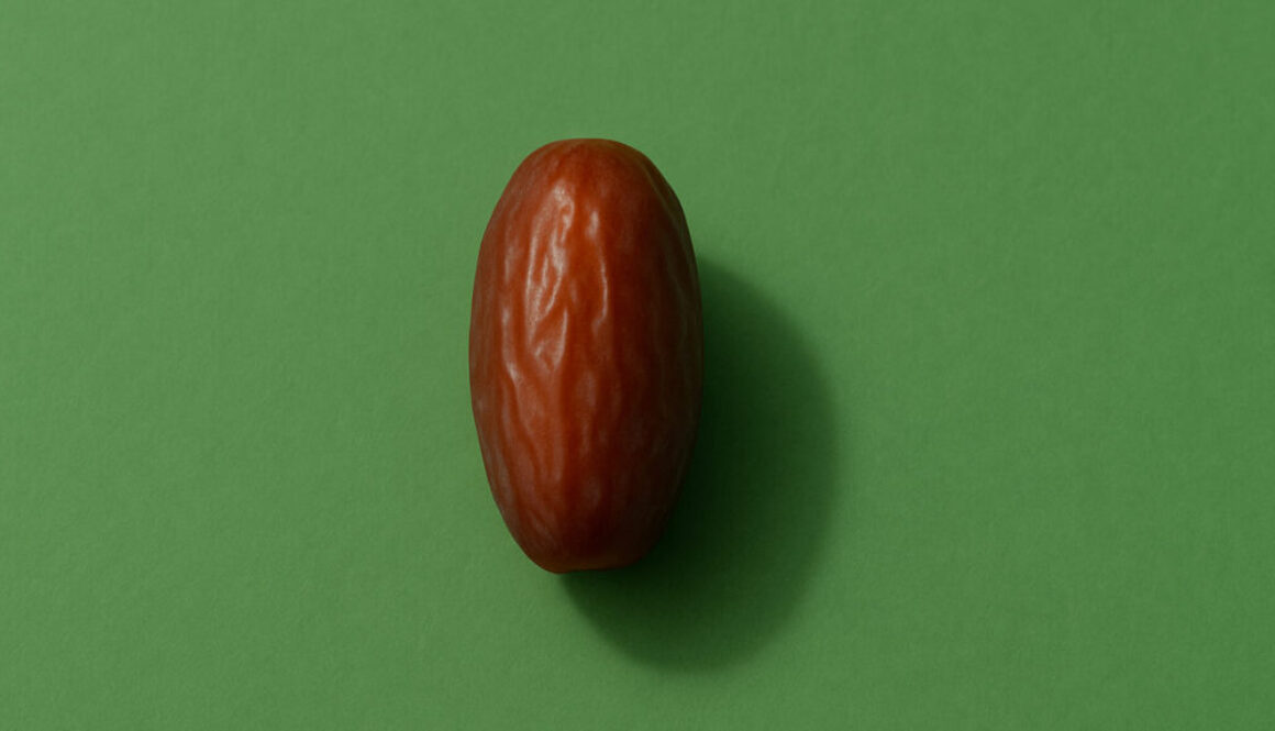 Minimal close-up of a single date fruit centered on green background in 16:9 format