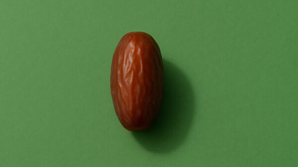 Minimal close-up of a single date fruit centered on green background in 16:9 format