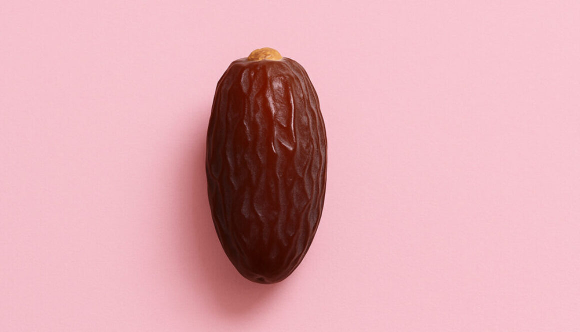 Minimal close-up of a single date fruit centered on pastel pink background in 16:9 format
