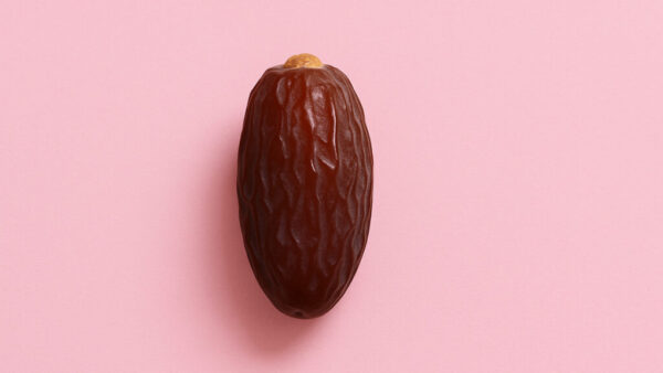 Minimal close-up of a single date fruit centered on pastel pink background in 16:9 format