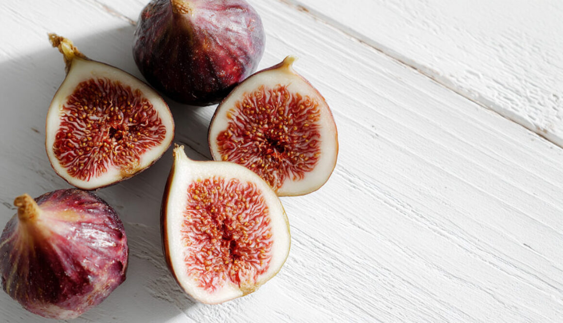 Flatlay top view of whole and cut figs on clean white wooden background in 16:9 format