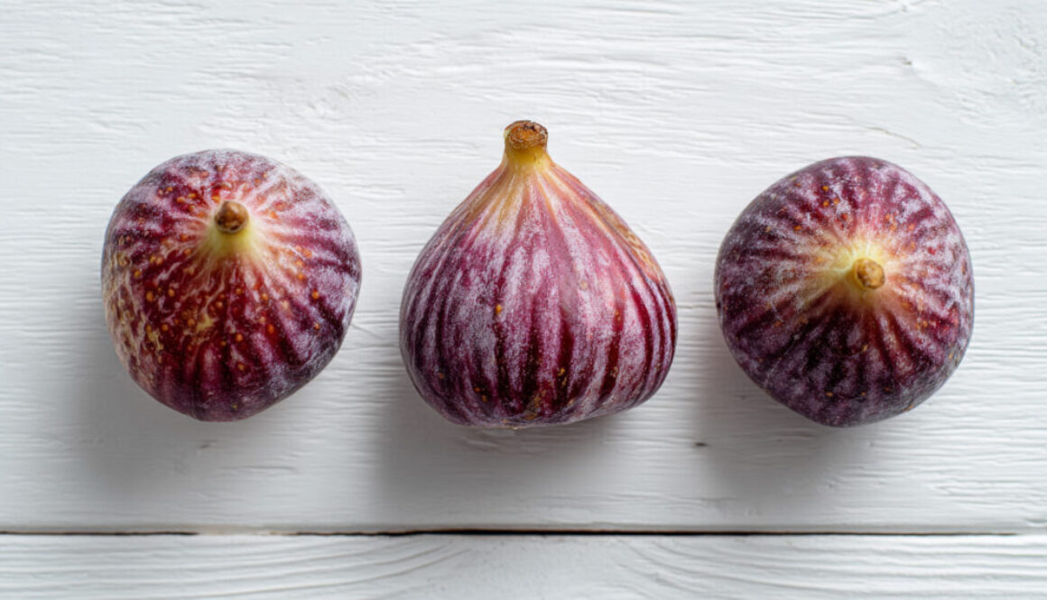 Flatlay top view of three ripe figs on clean white wooden background in 16:9 format