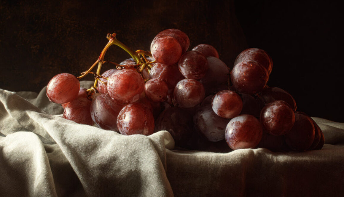 Rustic still life of red grapes on linen cloth with dark background in 16:9 format