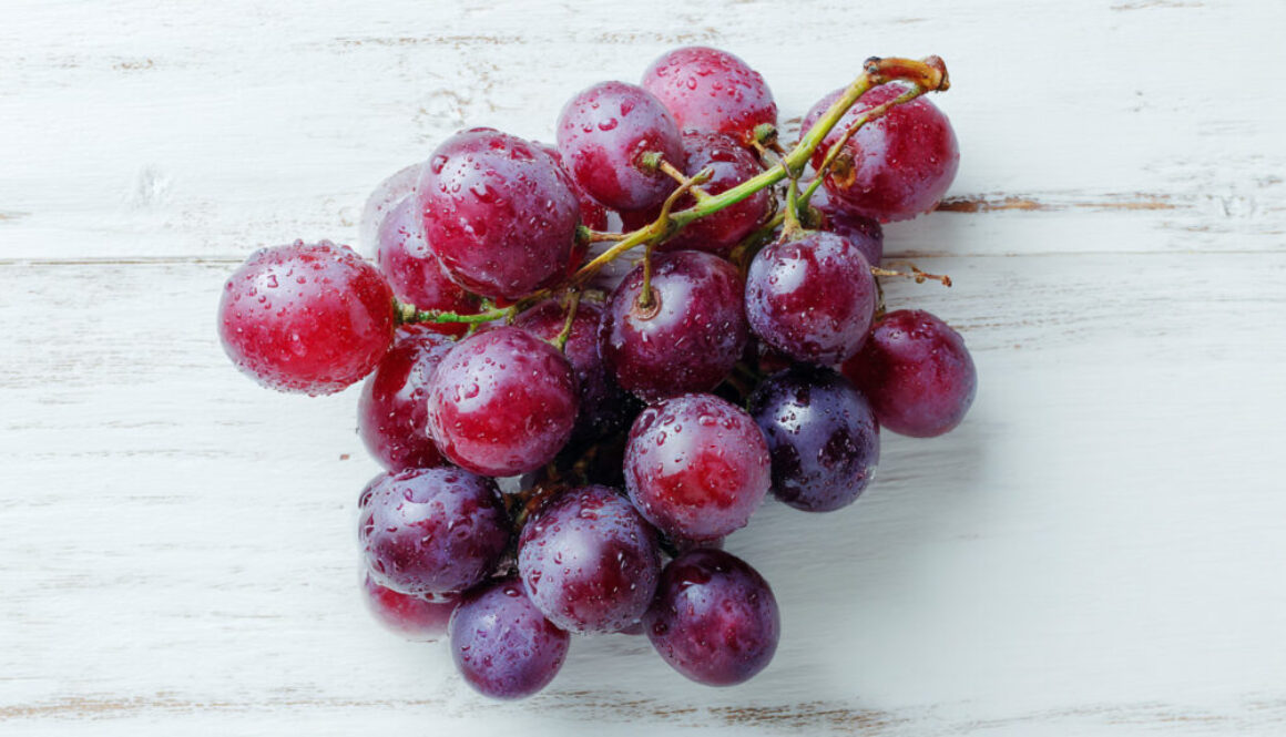 Flatlay of fresh red grapes with water drops on rustic white wooden background in 16:9 format