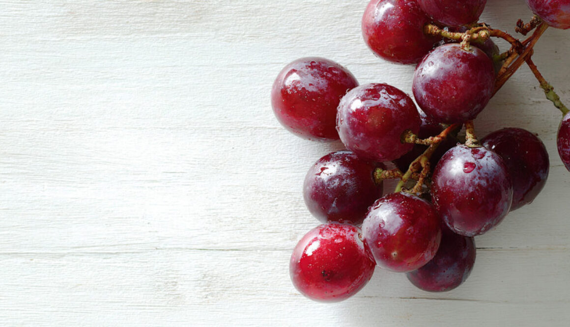 Flatlay of fresh red grapes with water drops on white wooden background in 16:9 format