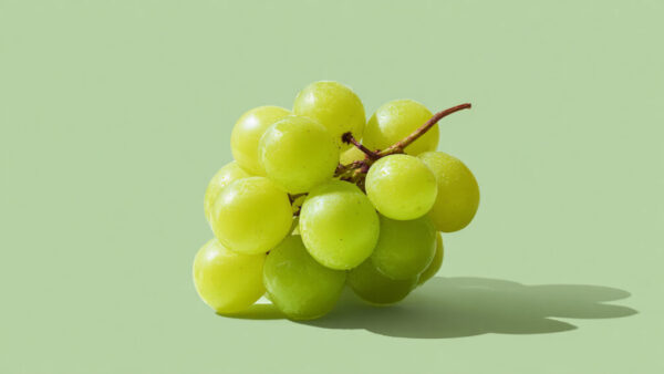 Fresh green grape cluster centered on light green solid background in 16:9 format