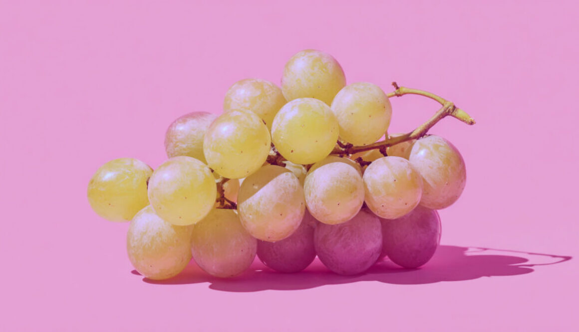 Bunch of fresh yellow grapes centered on solid pink background in 16:9 format