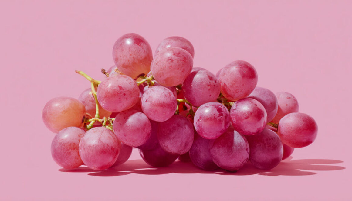 Cluster of fresh red-pink grapes centered on pastel pink background in 16:9 format