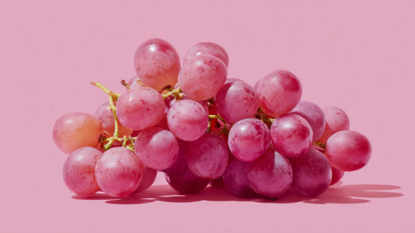 Cluster of fresh red-pink grapes centered on pastel pink background in 16:9 format