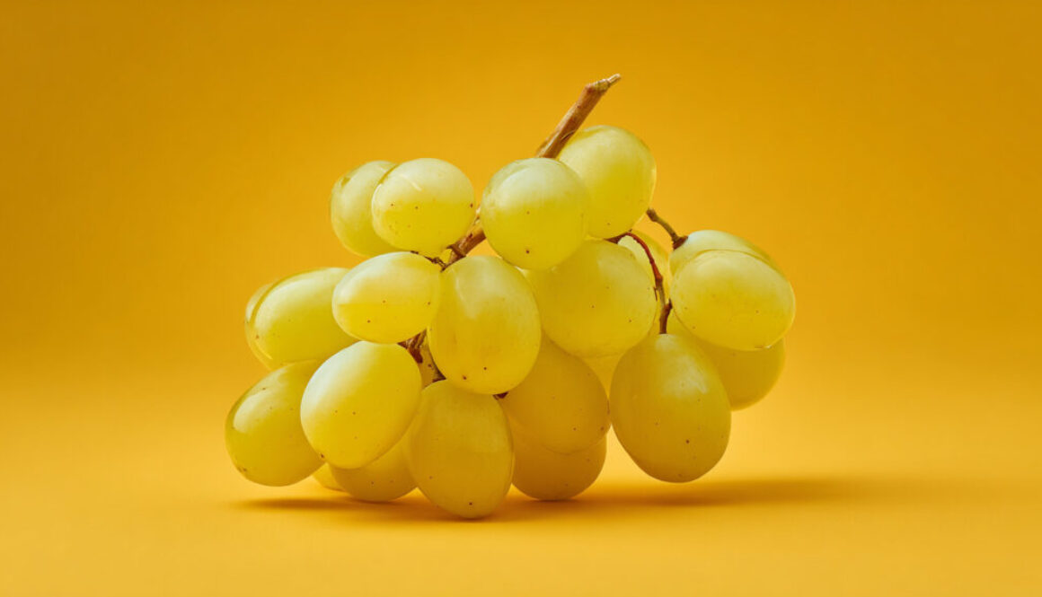Bunch of fresh yellow grapes centered on solid yellow background in 16:9 format
