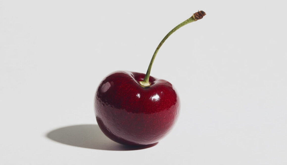 Minimal isolated cherry on a pure white background with sharp shadows, glossy red fruit photo in 16:9 format