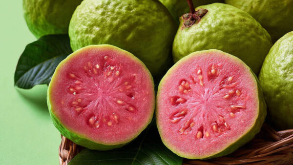 Close-up of sliced pink guava with seeds on green background in 16:9 format
