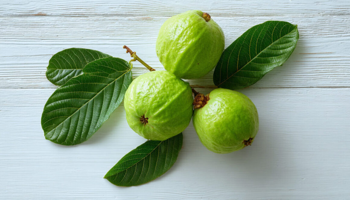 Flatlay of fresh green guavas with leaves on white wooden background in 16:9 format