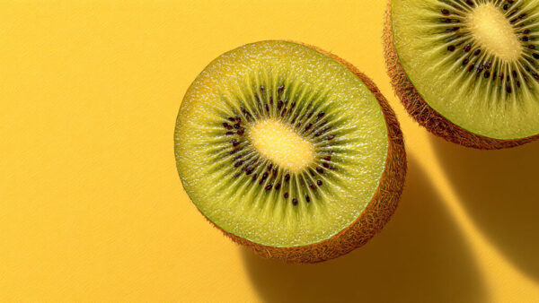 Half slices of fresh kiwi on vibrant yellow background