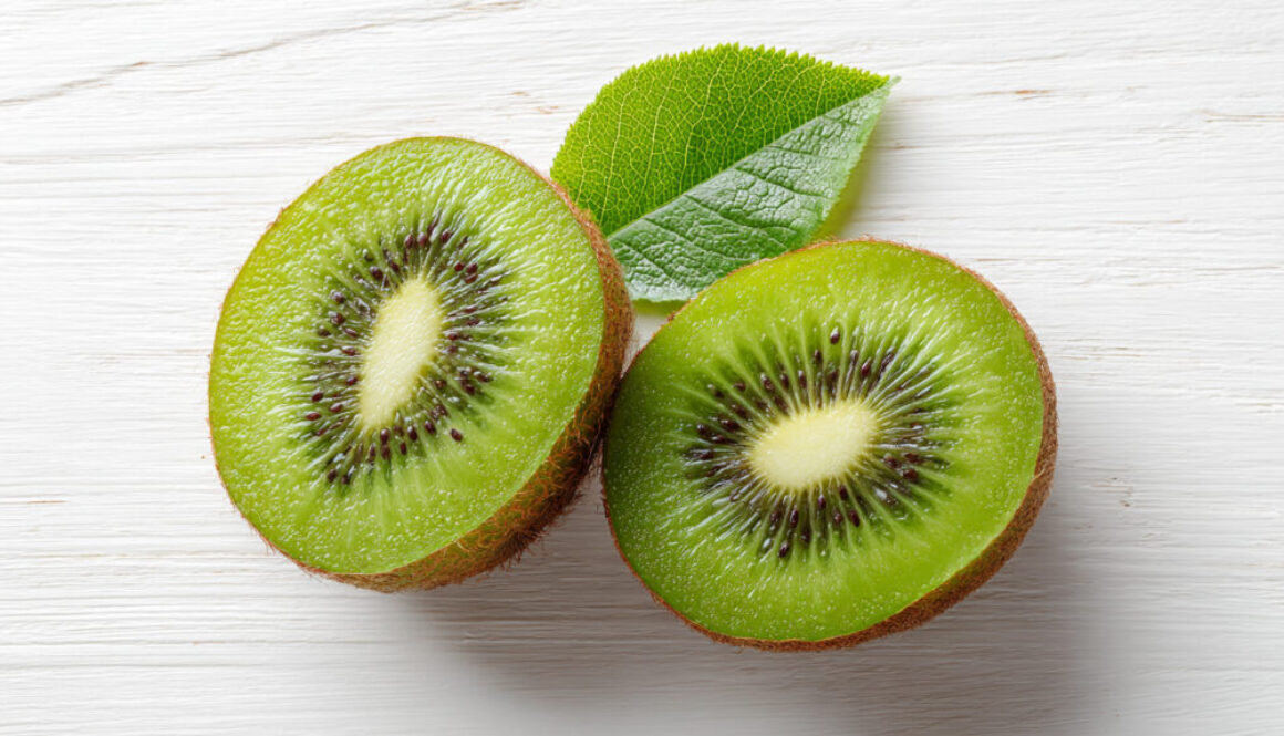 Flatlay of fresh kiwi halves with green leaf on clean white background