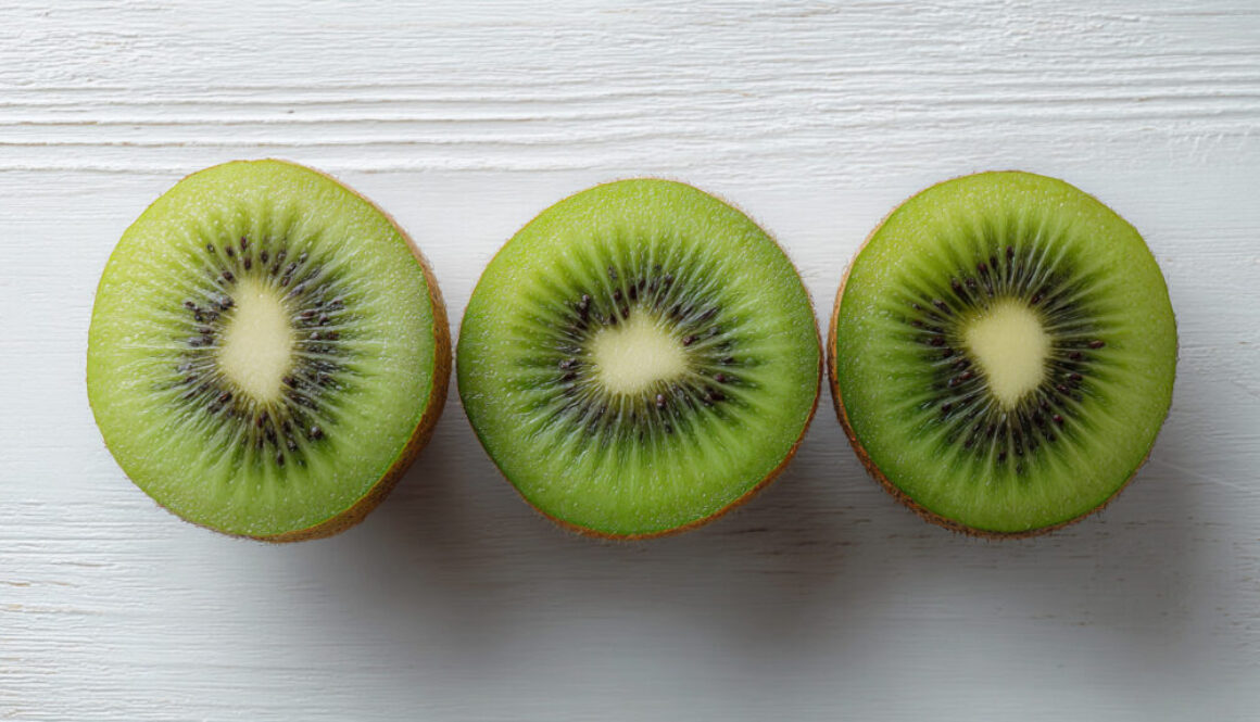 Flatlay of three kiwi halves arranged on clean white wooden background