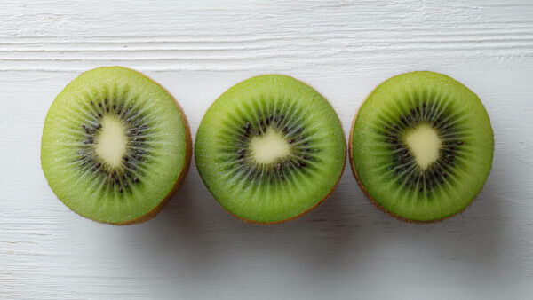 Flatlay of three kiwi halves arranged on clean white wooden background