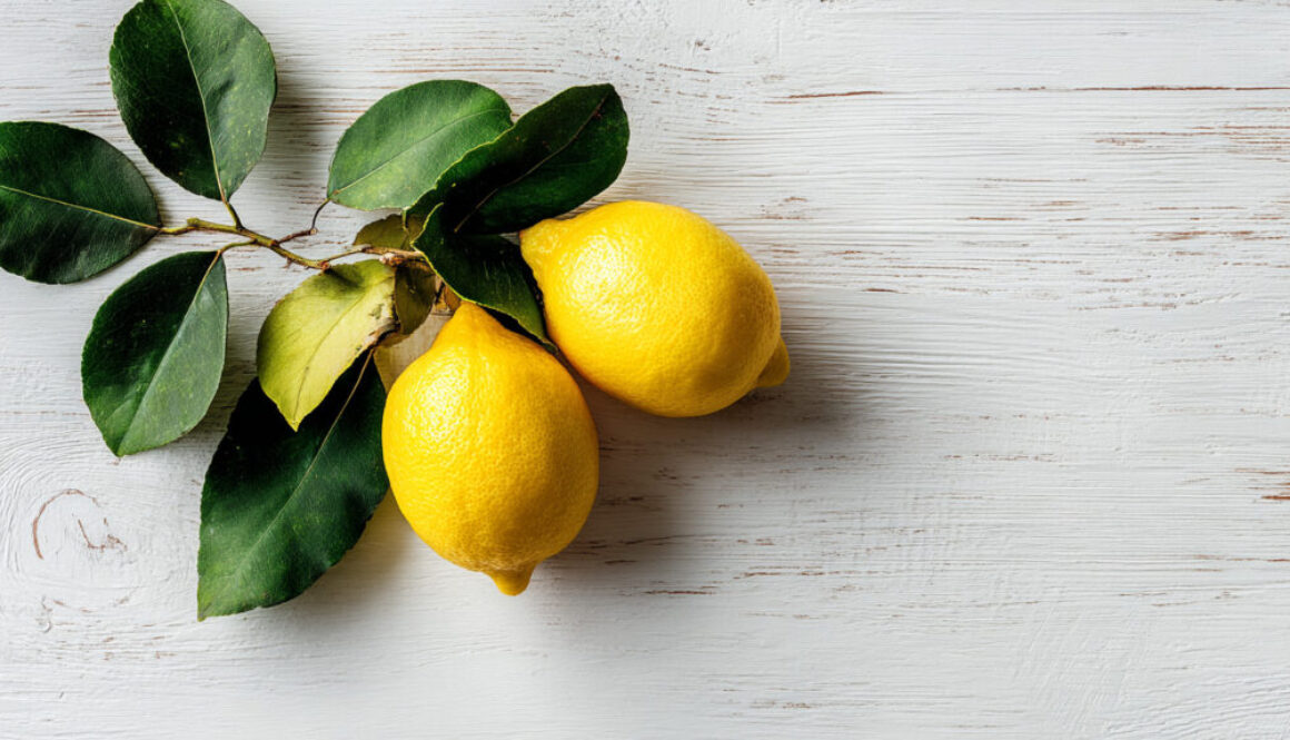 Flatlay of fresh lemons with green leaves on rustic white wooden background