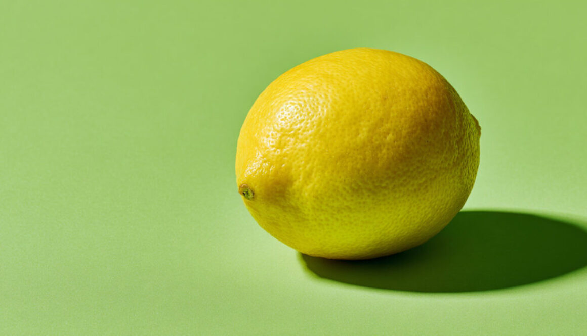 Single lemon centered on solid green background with shadow in 16:9 format