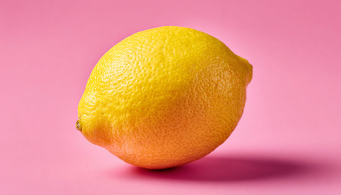 Single lemon centered on solid pink background with soft shadow in 16:9 format
