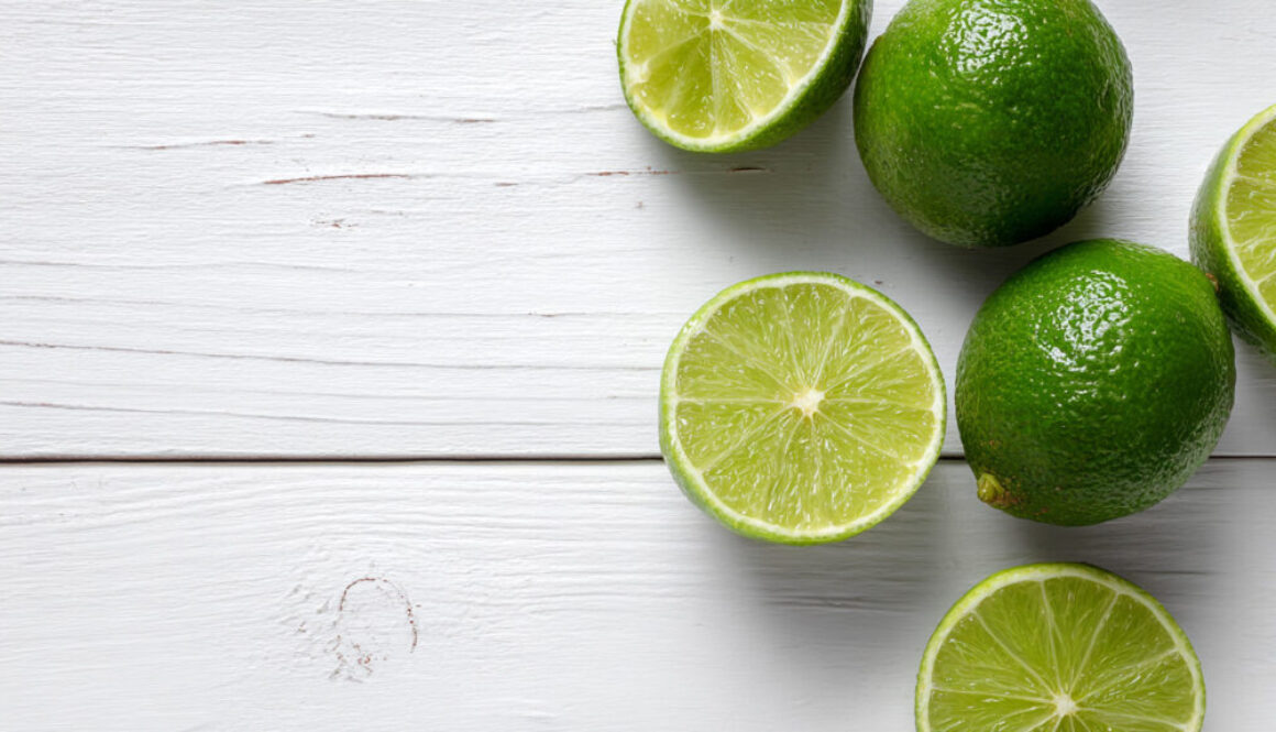 Top view of fresh whole and halved limes on white wooden background in 16:9 format