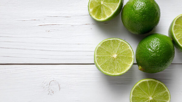 Top view of fresh whole and halved limes on white wooden background in 16:9 format