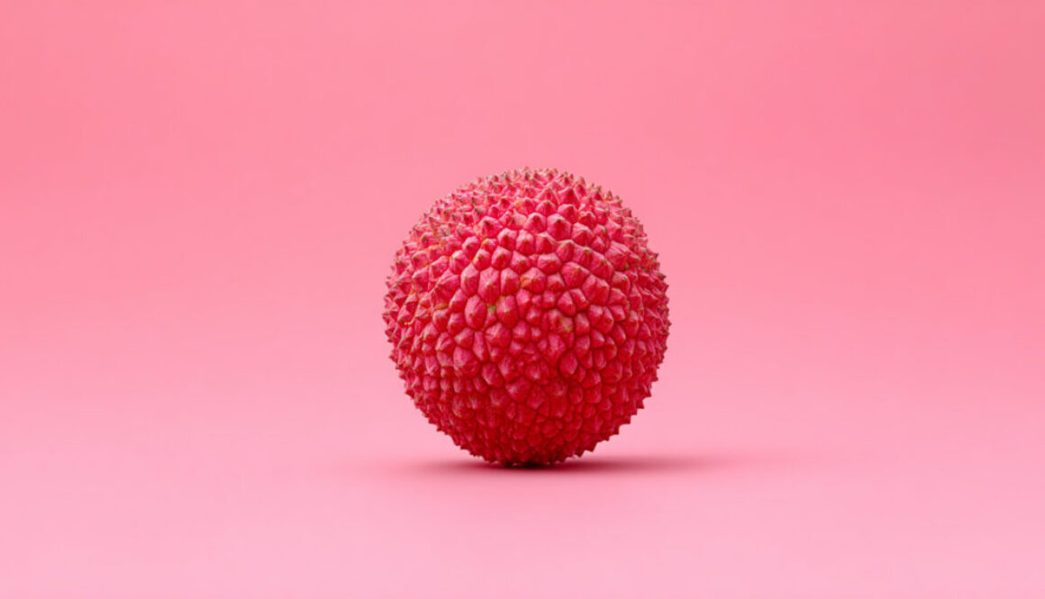 Front view of a single lychee fruit centered on a soft pink background in 16:9 format