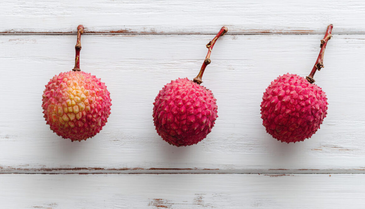 Flat lay of three lychees on white wooden background in 16:9 format