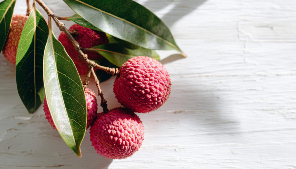Branch of fresh lychees with green leaves on white wooden background in 16:9 format